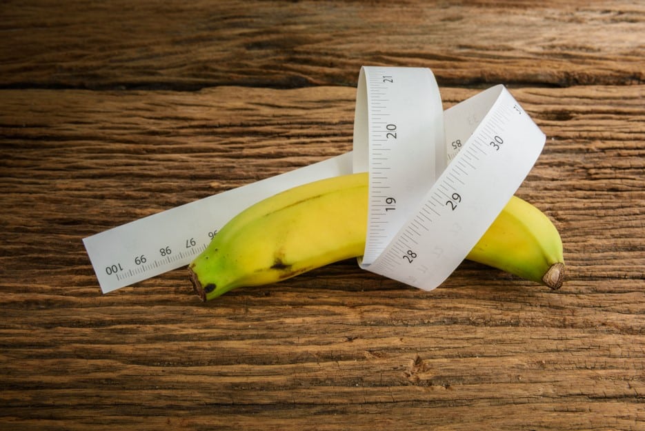 Banana sobre uma mesa de madeira e enrolada em uma fita métrica para representar maneiras de como desentortar o pênis.