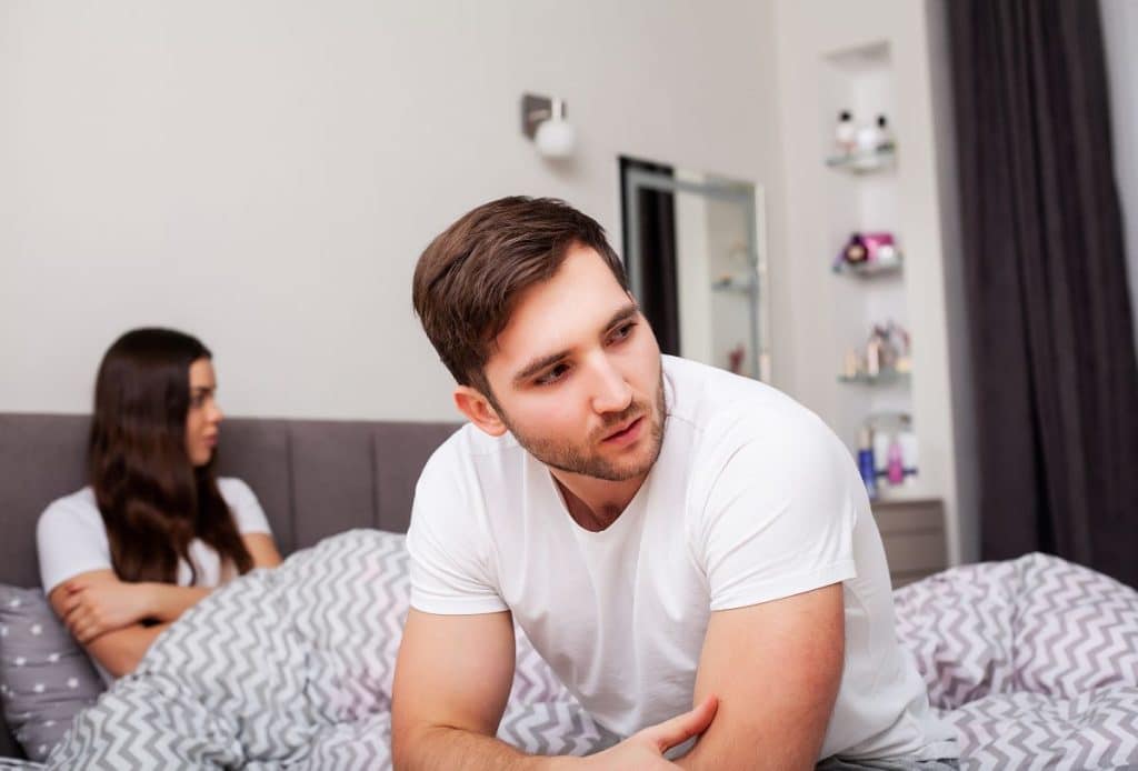 ovem casal em um quarto, aparentemente em meio a uma conversa séria ou um momento de tensão, falando sobre disfunção erétil em jovens. 