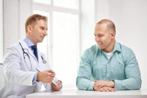 um médico e um paciente estão sentados frente a frente em um consultório médico, envolvidos em uma conversa.