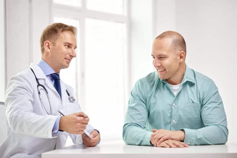 um médico e um paciente estão sentados frente a frente em um consultório médico, envolvidos em uma conversa.