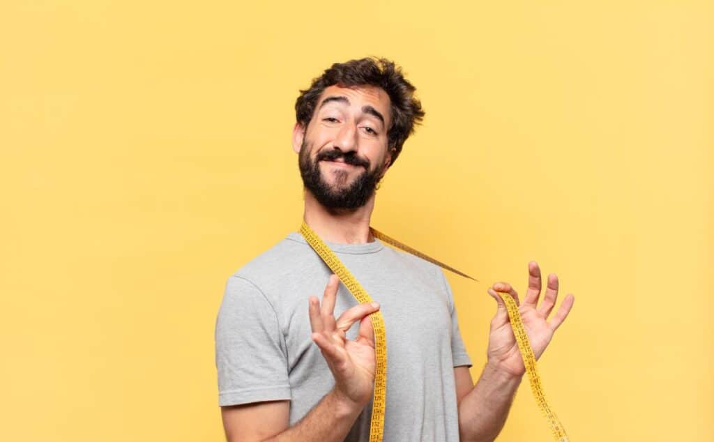 Homem confiante com fita métrica no ombro representa autoestima após tratamento com aumentador peniano.